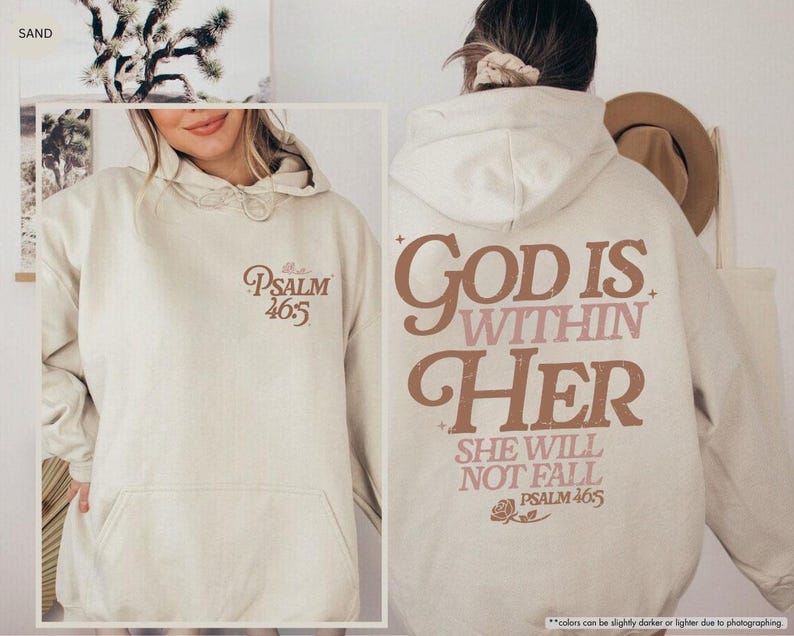Puede incluir: Sudadera con capucha color arena con bolsillo delantero y capucha con cord&oacute;n. La parte delantera presenta el texto "Psalm 46:5" en escritura marr&oacute;n. La parte trasera muestra "God is Within Her" y "She Will Not Fall" en letras marrones y rosas, con "Psalm 46:5" debajo.