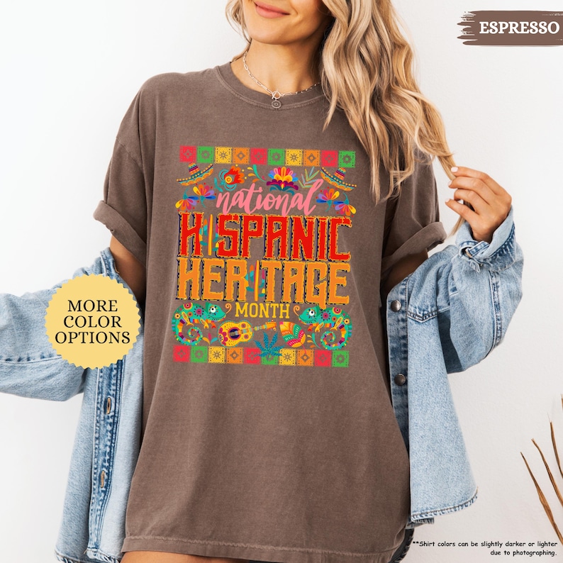 Peut inclure: T-shirt marron avec l'inscription "national HISPANIC HERITAGE MONTH" dans un design color&eacute;. Le t-shirt a un col rond et des manches courtes. Un bouton sur le c&ocirc;t&eacute; gauche indique "MORE COLOR OPTIONS".