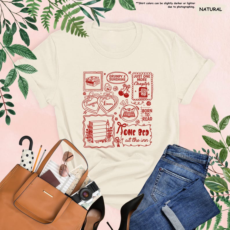 May include: Cream-colored t-shirt with a red graphic featuring book-themed illustrations and text. The design includes phrases like "Grumpy x Sunshine," "Just One More Chapter," and "Born to Read." The shirt is paired with blue jeans and a brown handbag.