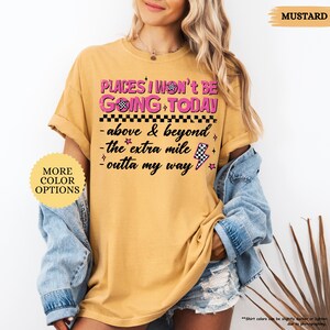 May include: Mustard-colored t-shirt with the text "PLACES I WON'T BE GOING TODAY" in pink and black. The shirt also features the phrases "above & beyond", "the extra mile", and "outta my way".