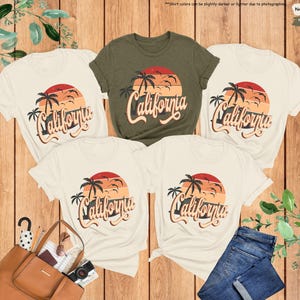 May include: Four t-shirts with a vintage California sunset graphic. The shirts are in various colors, including white, olive green, and heather olive. The text "California" is written in a retro font.