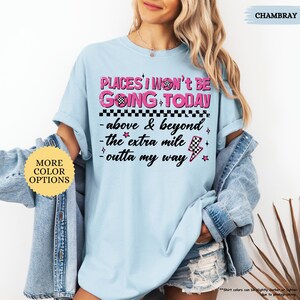 May include: Light blue t-shirt with the text "PLACES I WON'T BE GOING TODAY" in pink and black. The shirt also features the phrases "above & beyond", "the extra mile", and "outta my way". A denim jacket is draped over the shirt.