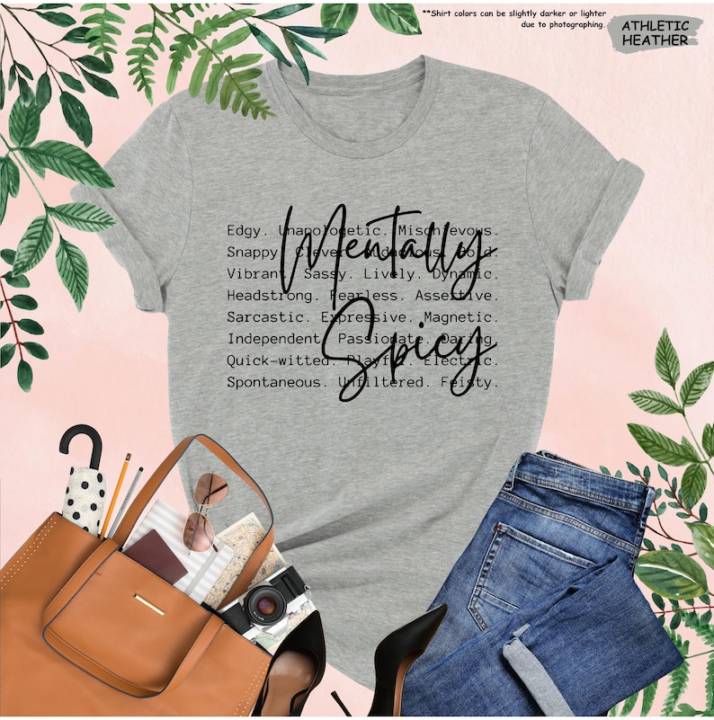 K&ouml;nnte beinhalten: Graues Athletic Heather T-Shirt mit dem Schriftzug "Mentally Spicy" in schwarzer Schrift. Das Shirt listet auch Adjektive wie "Edgy", "Sassy" und "Fearless" auf. Das Bild zeigt auch eine blaue Jeans, eine braune Handtasche und schwarze High Heels.