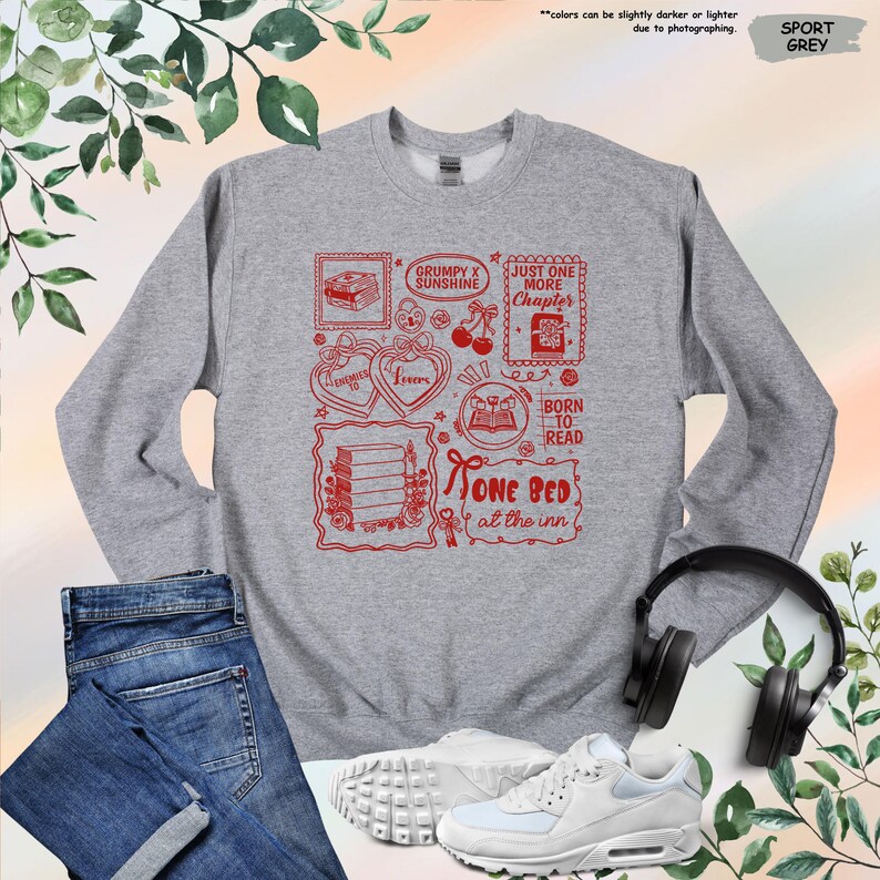 May include: Sport grey sweatshirt with a red graphic design featuring book-themed illustrations and text. The text includes phrases like "Grumpy x Sunshine," "Just One More Chapter," and "Born to Read."