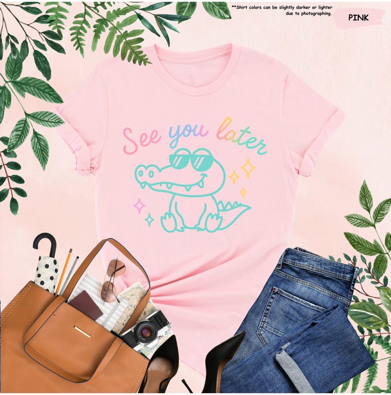 May include: A pink t-shirt with the phrase "See you later" and a cartoon alligator wearing sunglasses. The shirt is paired with blue jeans, a brown handbag, and black heels. Green leaves and foliage surround the items.
