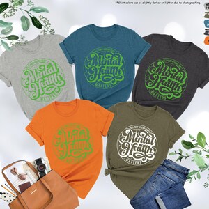 May include: Five t-shirts in different colors with a green graphic that says "Mental Health Matters" in a retro font.