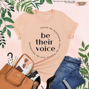 a t - shirt that says be their voice next to a handbag and purse