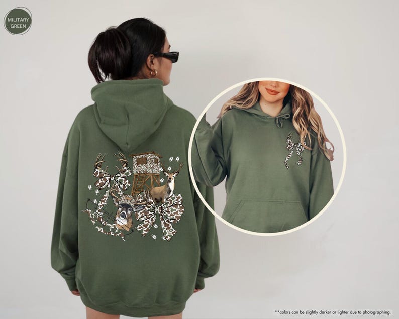 May include: A military green hoodie featuring a deer-themed graphic on the back, including deer, a hunting blind, and camouflage bows. The front of the hoodie has a small bow graphic. The hoodie has a hood and a front pocket.