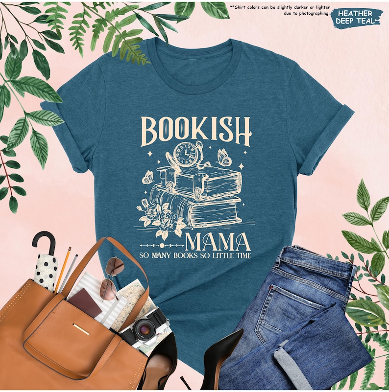 May include: A teal t-shirt with the words "BOOKISH MAMA" in a cream-colored font, along with an illustration of books, a clock, and butterflies. The text "SO MANY BOOKS SO LITTLE TIME" is below the illustration. The shirt is paired with jeans and a brown tote bag.