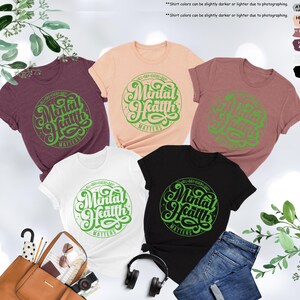 May include: Five different color t-shirts with a green graphic that says "All Day Every Day Mental Health Matters".