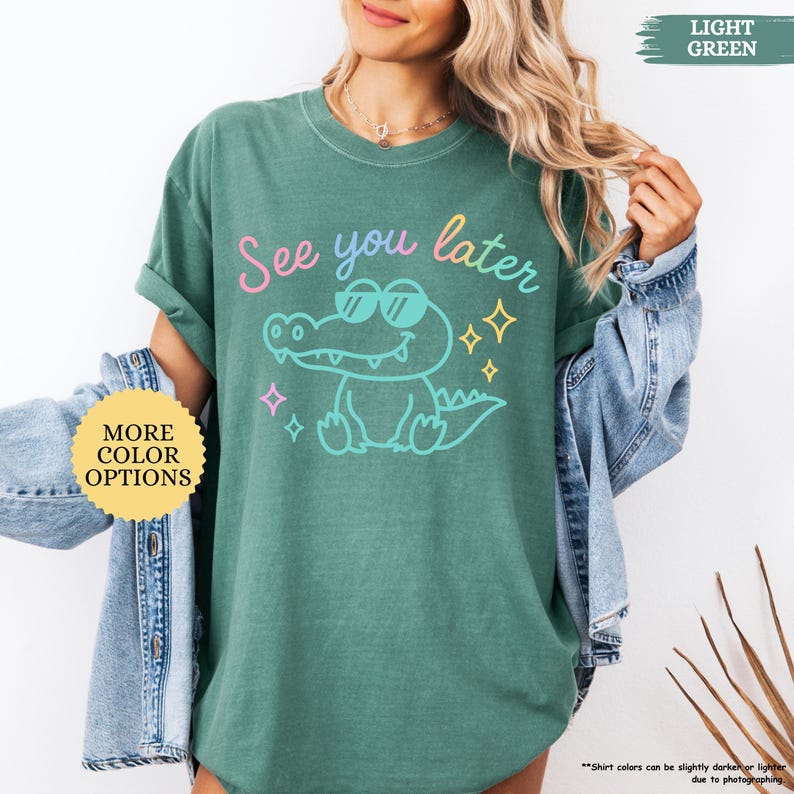 Puede incluir: Una camiseta verde claro con la frase "See you later" y un cocodrilo de dibujos animados con gafas de sol. La camiseta tambi&eacute;n tiene un bot&oacute;n que dice "M&aacute;s opciones de color".