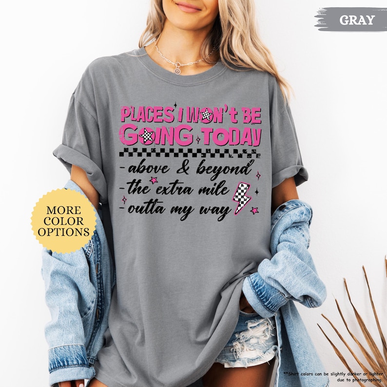 May include: Gray t-shirt with the text "PLACES I WON'T BE GOING TODAY" in pink and black. The shirt also features the phrases "above & beyond", "the extra mile", and "outta my way". A yellow circle with "MORE COLOR OPTIONS" is in the image.