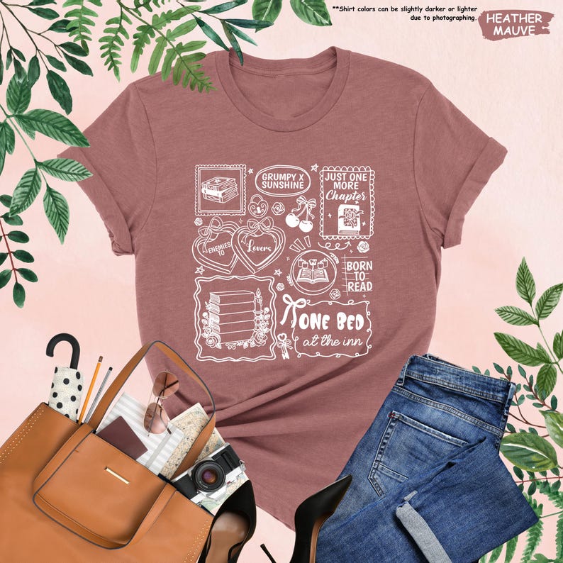 May include: Heather mauve t-shirt with a white graphic design featuring book-themed illustrations and text. The design includes the phrases "Grumpy x Sunshine", "Just One More Chapter", "Born to Read", and "One Bed at the Inn".