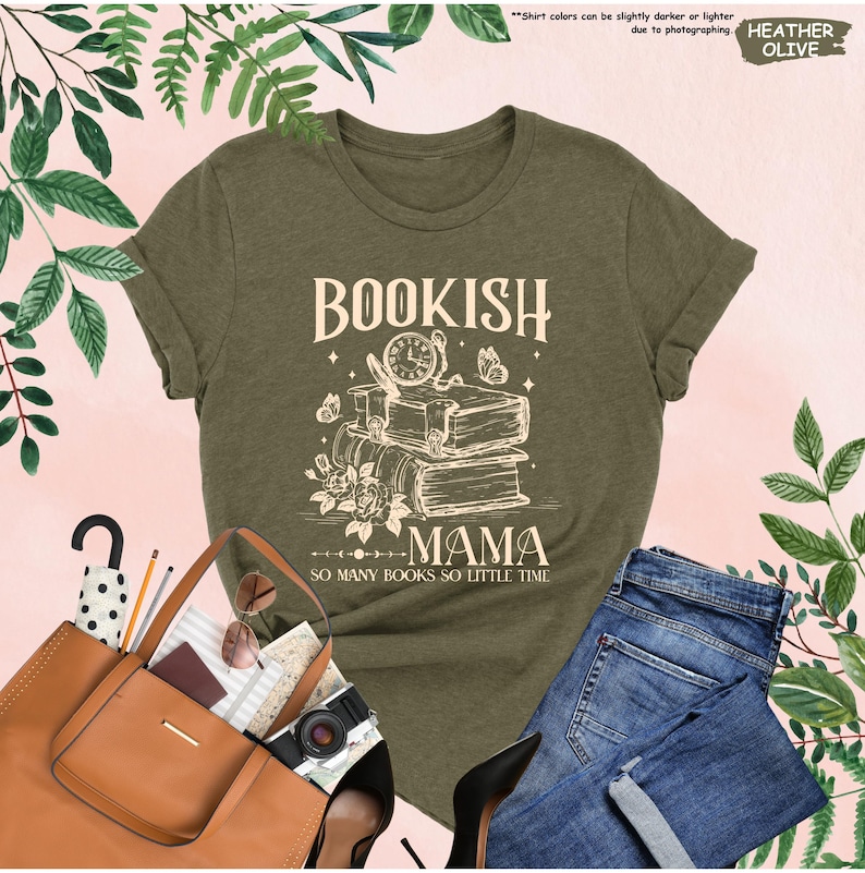 May include: Heather olive green t-shirt with the text "BOOKISH MAMA" and "SO MANY BOOKS SO LITTLE TIME". The graphic includes a stack of books, a clock, butterflies, and flowers. The shirt is paired with blue jeans and a brown tote bag.