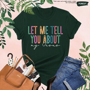 May include: A dark green t-shirt with the text "LET ME TELL YOU ABOUT my Jesus" in rainbow colors. The text is in a retro font style.