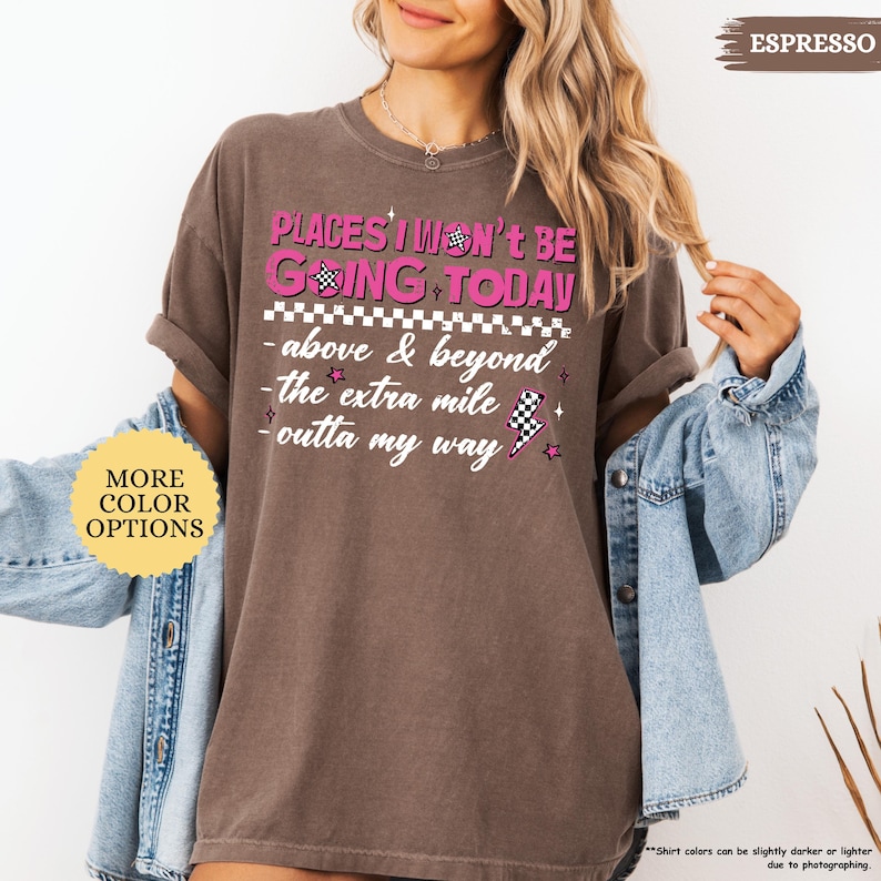 May include: Espresso-colored t-shirt with the text "PLACES I WON'T BE GOING TODAY" in pink and white. The shirt features a checkered flag design and additional phrases like "above & beyond" and "outta my way".