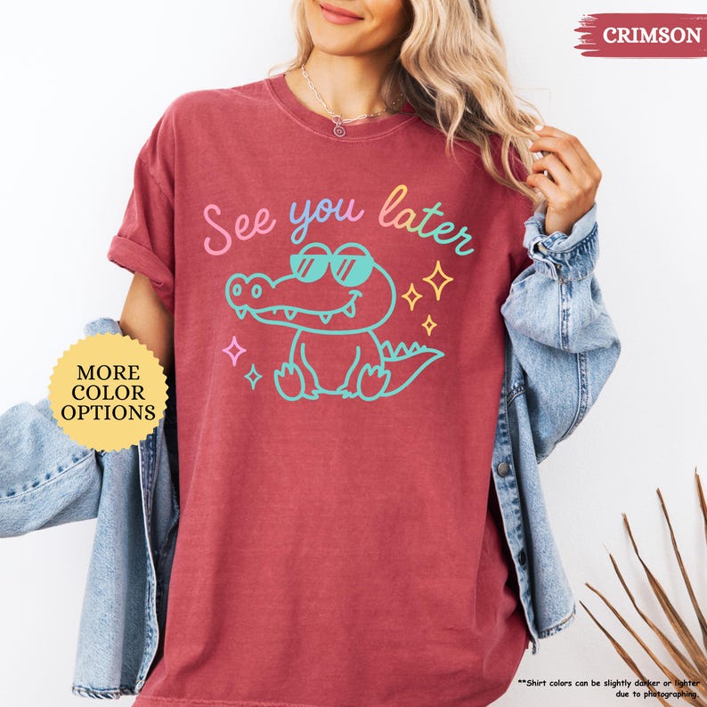 Puede incluir: Camiseta de color carmes&iacute; con un cocodrilo de dibujos animados con gafas de sol y el texto "See you later". El dise&ntilde;o est&aacute; en una fuente colorida con estrellas. La camiseta tiene cuello redondo y mangas cortas. "More Color Options" es visible.