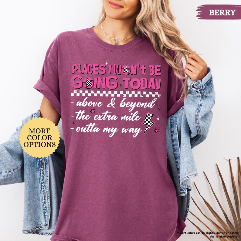 May include: Berry-colored t-shirt with the text "PLACES I WON'T BE GOING TODAY" in pink. The design includes a checkered flag, stars, and lightning bolt graphics. The shirt also has the phrases "above & beyond", "the extra mile", and "outta my way".