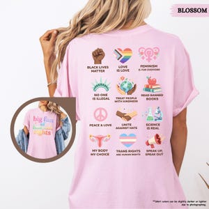May include: A light pink t-shirt with various social justice icons and phrases printed on the back, including "Black Lives Matter," "Love is Love," and "Trans Rights are Human Rights." The front of the shirt features the text "big fan of human rights."