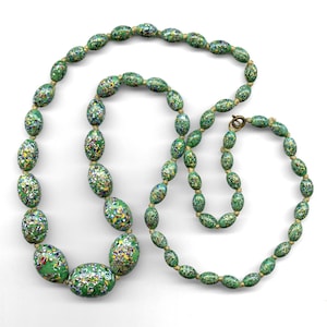 May include: A long green and gold necklace with oval-shaped beads. The beads are covered in a speckled pattern of green, gold, and white.