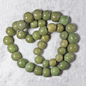 May include: A strand of green beads made of natural materials. The beads are round and have a smooth, polished finish.