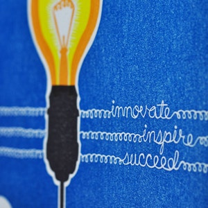 May include: A yellow light bulb with a black base and a white cord. The cord has the words "innovate", "inspire", and "succeed" written on it.