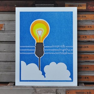 May include: A blue and white print with a yellow light bulb, white clouds, and the text "innovate inspire succeed".
