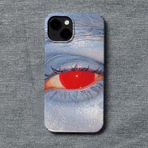 Pode incluir: Capa de telemóvel com um close-up de um olho com íris vermelho brilhante e longos cílios. O olho está sobre um fundo azulado, criando um contraste marcante. A capa tem um acabamento brilhante.