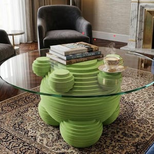 Puede incluir: Un salón moderno con una mesa de centro única. La mesa tiene una tapa redonda de vidrio transparente sostenida por una base escultural verde lima. Una pila de libros y una taza de té están sobre la mesa. La habitación incluye sillones y una alfombra estampada.