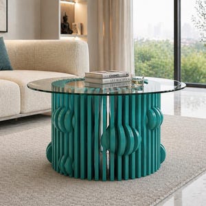 May include: A modern coffee table with a round glass top and a teal base. The base features vertical slats and decorative circular accents. Books are stacked on the table. The table is in a living room setting.
