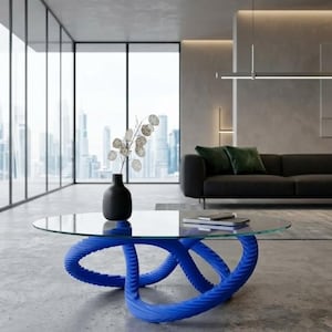 Puede incluir: Salón moderno con una mesa de centro azul escultural con tapa de cristal. Un jarrón negro con ramas decorativas está sobre la mesa. Un sofá negro con cojines verdes y una vista de la ciudad son visibles en el fondo.