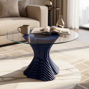 May include: A modern coffee table with a clear glass top and a navy blue, wave-like base. A beige mug and an open magazine rest on the table. The table sits on a marble-patterned surface.