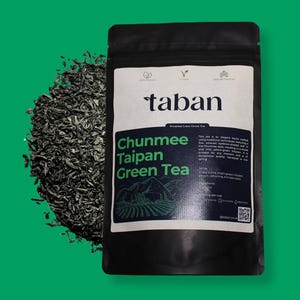 May include: A black pouch with a white label that reads "taban Premium Loose Green Tea" and "Chunmee Taipan Green Tea". The label also features a green illustration of a tea plantation. The pouch is filled with loose green tea leaves.