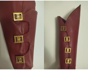 May include: Close-up of a red leather boot with gold metal buckles. The boot has a pointed toe and a high heel.