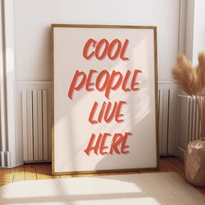May include: A framed print with the text "COOL PEOPLE LIVE HERE" in a bold, red font on a light pink background.