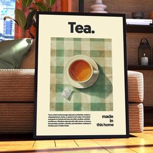 May include: A framed poster with the word "Tea." in bold black text. The poster features a green and white checkered tablecloth with a cup of tea and a tea bag on a white saucer. The text below the image reads "Tea is a beloved beverage enjoyed worldwide, made by steeping leaves, herbs, or spices in hot water. From black and green tea to herbal and chai, tea offers endless varieties and flavors.  With countless ways to enjoy it, with milk, lemon, or honey, tea provides comfort, warmth, and relaxation, making it a timeless part of daily rituals. Made in this home."