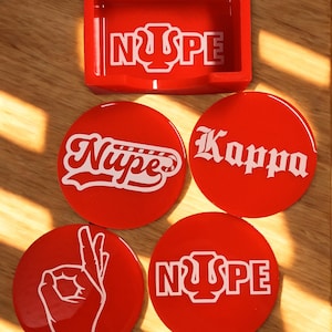 May include: A red ashtray and four red coasters with white lettering and graphics. The ashtray and two coasters have the text "NΨSPE". One coaster has the word "Kappa", and another has the word "Nüpe". The last coaster has a hand gesture.
