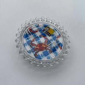 Puede incluir: Plato de cristal transparente con dise&ntilde;o de cangrejo y fondo a cuadros azules y blancos. El plato tiene un borde con cuentas y presenta el texto "Old Bay Seasoning".