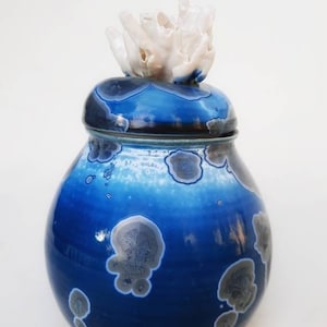 May include: A blue and white ceramic jar with a white coral-like lid. The jar has a speckled blue and white glaze with a mottled effect.