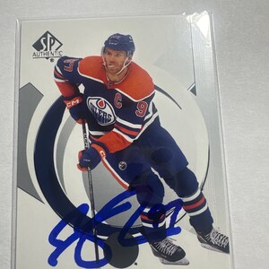 May include: SP Authentic hockey card featuring Connor McDavid in an Edmonton Oilers uniform. The card has a blue autograph and the player's name and team logo are visible. The card is encased in a protective sleeve.