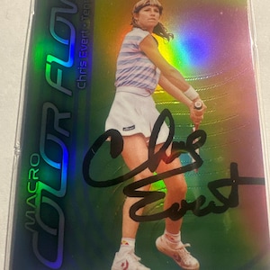 Puede incluir: Una tarjeta comercial Macro Color Flow Allure con la tenista Chris Evert. La tarjeta tiene un fondo holográfico con una foto de Evert con ropa de tenis, sosteniendo una raqueta. Su firma es visible.