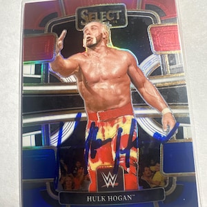 Puede incluir: Tarjeta coleccionable con Hulk Hogan en una pose de lucha libre. La tarjeta tiene un fondo holográfico con la palabra "Select" en la parte superior. Hogan lleva un calzón de lucha libre rojo y amarillo y una firma. El logotipo de la WWE es visible.