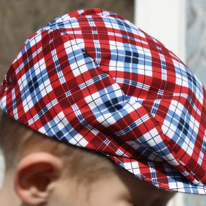 Puede incluir: Una gorra de newsboy de cuadros rojos, blancos y azules con una visera curva.