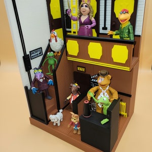 May include: A multi-level playset featuring characters from the Muppets, including Miss Piggy, Kermit the Frog, Fozzie Bear, and Animal. The playset includes a dressing room, a stage, and a control room. The playset is made of plastic and is painted in bright colors.