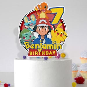 Op de afbeelding: Een witte cake met een rode, witte en blauwe Pokemon-thema caketopper. De topper toont Pikachu, Bulbasaur, Charmander, Squirtle en een trainer. De caketopper zegt "Benjamin Birthday".