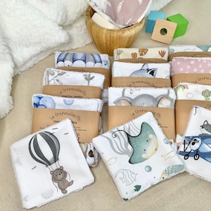 Peut inclure: Un ensemble de débarbouillettes pour bébés avec divers motifs sur le thème des animaux et de la nature. Les débarbouillettes blanches présentent des illustrations colorées d'un ours en montgolfière, d'une raie et d'autres animaux. Le texte "La Grenouillette" est imprimé sur l'emballage.