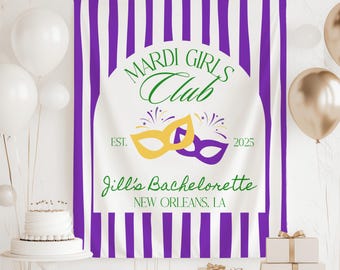 May include: Purple and white striped backdrop with the text "Mardi Girls Club Est. 2025" and "Jill's Bachelorette New Orleans, LA". Two gold and purple masquerade masks are in the center of the backdrop.
