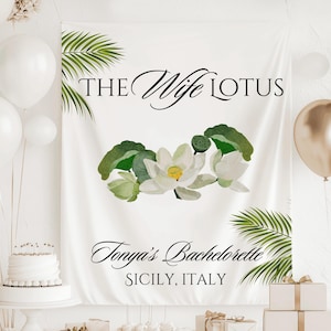 May include: White backdrop with green palm leaves and a white lotus flower design. The text "The Wife Lotus" is at the top of the backdrop. The text "Tonya's Bachelorette Sicily, Italy" is at the bottom of the backdrop.