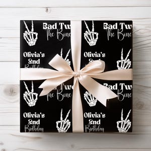 May include: Black and white wrapping paper with a skeleton hand peace sign and the text "Bad Two The Bone" and "Olivia's 2nd Birthday".