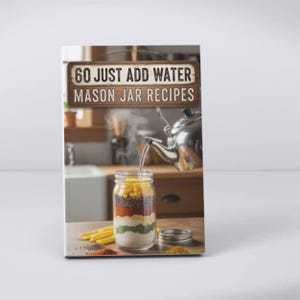 Pu&ograve; includere: Un libro di cucina intitolato "60 Just Add Water Mason Jar Recipes" presenta un barattolo Mason a strati con ingredienti. Una teiera d'argento versa acqua nel barattolo. Il libro &egrave; su una superficie chiara con spezie e ingredienti.